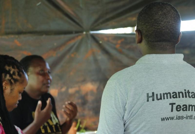 Gruppsamtal på humanitär konferens i Kenya 2020. Tre personer samtalar under en konferens i Kenya. På mannen vänd bort från kameran ser man texten Humanitarian Team på hans rygg.