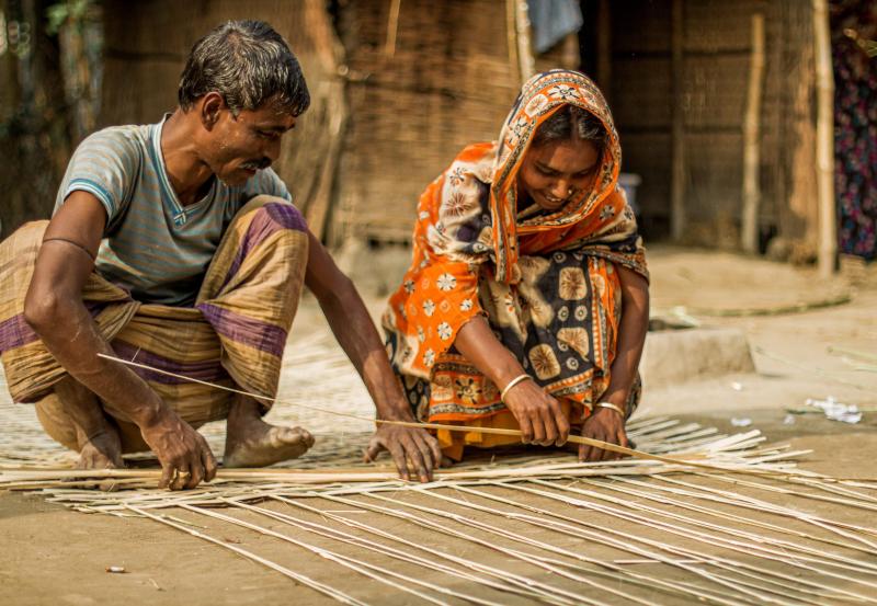 Korgflätning i Bangladesh pågår. En kvinna och en man från Bangladesh sitter på huk och flätar en korg tillsammans.