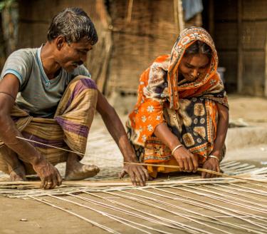 Korgflätning pågår. En kvinna och en man från Bangladesh flätar en korg tillsammans